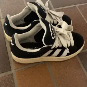 Snygga svarta Adidas campus i storlek 37  sneakers med vita detaljer och snörning. Klassisk design med tre ränder på sidan och en bekväm sula. Perfekta för en avslappnad stil.