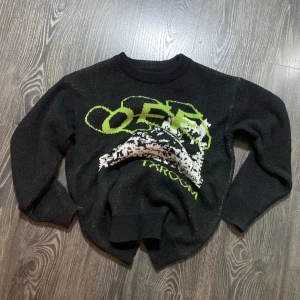 Svart tröja med grafiskt tryck/broderi - Cool svart tröja med ett unikt grafiskt tryck i grönt och vitt. Perfekt för en avslappnad stil. Tröjan har långa ärmar och en rund halsringning. Har ingen lapp vid nacken. FAK3? Priset kan diskuteras!