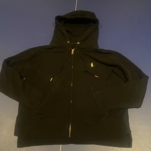 Svart hoodie från Polo Ralph Lauren - Säljer en stilren svart hoodie från Polo Ralph Lauren med dragkedja och det klassiska broderade logotypen på bröstet. Perfekt för en avslappnad look. Dessutom en unik design på baksidan av hoodien där det sticker ut lite, Jag har fått många komplimanger på denna detalj! Nypris 2159. Som vanligt alltid öppen för prisförslag!