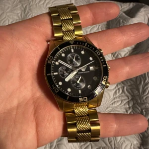 Armani klocka - Säljer en snygg guldfärgad klocka från Emporio Armani med svart urtavla och flera små urtavlor för extra funktioner. Armbandet är i metall med guldfärg. Säljer billigt eftersom den inte tickar längre och säkert behöver nytt bateri.