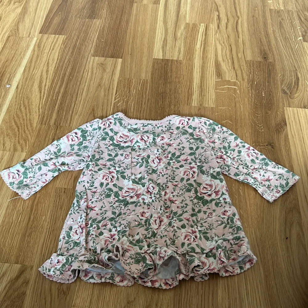 Söt blommig klänning i rosa och grönt från Tiny One. Tillverkad i ekologisk bomull med trekvartsärmar och volangdetaljer. Perfekt för små fashionistas!. Mekot.