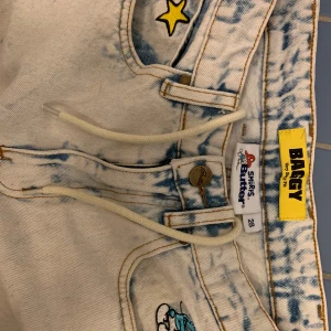 Baggy jeans med tryck från Butter Goods - Säljer ett par coola baggy jeans från Butter Goods i ljusblått med unika tryck av stjärnor och texten 'Butter' med cool smurf på. Använda och tvättade ett fåtal gånger. 
