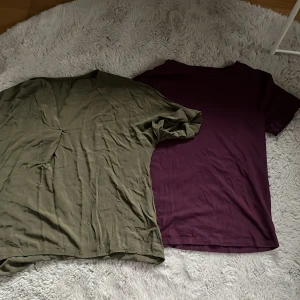 Två t-shirts i grönt och lila - Säljer två t-shirts i olika färger. Den ena är olivgrön och den andra är mörklila. Båda har en enkel design med korta ärmar och normal passform. Perfekta för vardagsbruk eller avslappnade tillfällen. Materialet känns mjukt och bekvämt.