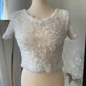 Vit fluffig topp från Accomplice - Superfin vit fluffig topp från Accomplice i storlek S. Den är kortärmad och har en mysig, lurvig textur som gör den perfekt för både fest och vardag. Tillverkad i 100% polyester, vilket gör den lätt och bekväm att bära. Perfekt för att ge din outfit en unik touch! ✨