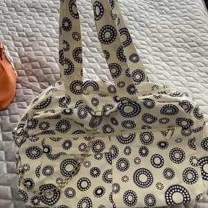 Vit och blå mönstrad väska OANVÄND  - Säljer en superfin vit väska Oanvänd med blå prickmönster. Den har två rejäla handtag och en dragkedja upptill. Perfekt för en dag på stan eller som en unik accessoar till din outfit. Väskan har också en kedjedetalj som ger den lite extra stil.