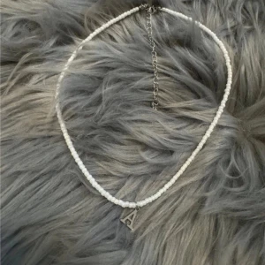 Vitt pärlhalsband bokstav A - Elegant vitt pärlhalsband med en bokstavsberlock i silver. Perfekt för att ge en personlig touch till din stil. Justerbar kedja för optimal passform. Bokstaven A