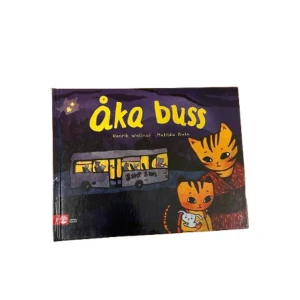 Åka buss - En charmig barnbok med titeln 'Åka buss' av Henrik Wallnäs och Matilda Ruta. Boken har ett färgglatt omslag med en tecknad katt och en buss i bakgrunden. Perfekt för barn som älskar äventyr och djur!
