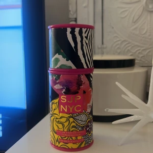 SJP NYC Eau de Parfum - Säljer en färgglad och stilren parfym från SJP NYC. Flaskan är genomskinlig med en guldig spraypump och kommer i ett coolt fodral med zebra- och blommönster i rosa, gult och grönt. Perfekt för dig som vill ha en doft med attityd och stil! 🌸🗽60ml ungefär kvar