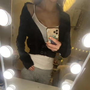 Svart kofta  - En svart kofta med knappar längst ner. Man kan ha den både öppen och med knapparna men det är bara knappar längst ner. Den är storlek xs och lite längre i armarna så den går över händerna vilket jag tycker är fint.