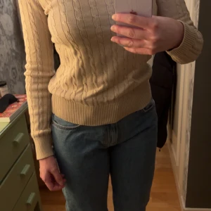 Beige stickad tröja från Boomerang - Säljer en stilren beige stickad tröja från Boomerang. Tröjan har ett klassiskt flätmönster och långa ärmar med ribbade muddar. I mycket bra skick!