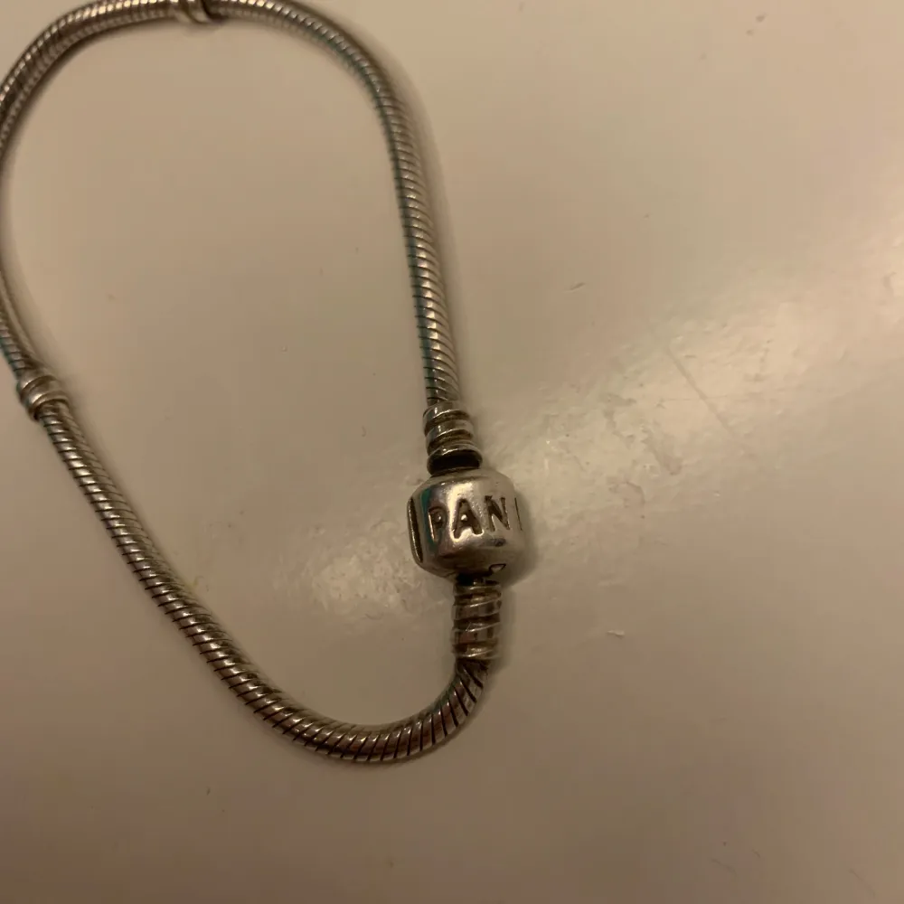 Säljer ett elegant silverarmband från Pandora i mycket bra skick. Armbandet har en klassisk design med en rund låsdetalj där Pandora är ingraverat. Perfekt för att bära ensam eller med berlocker för en personlig touch. Passar till både vardag och fest!. Accessoarer.