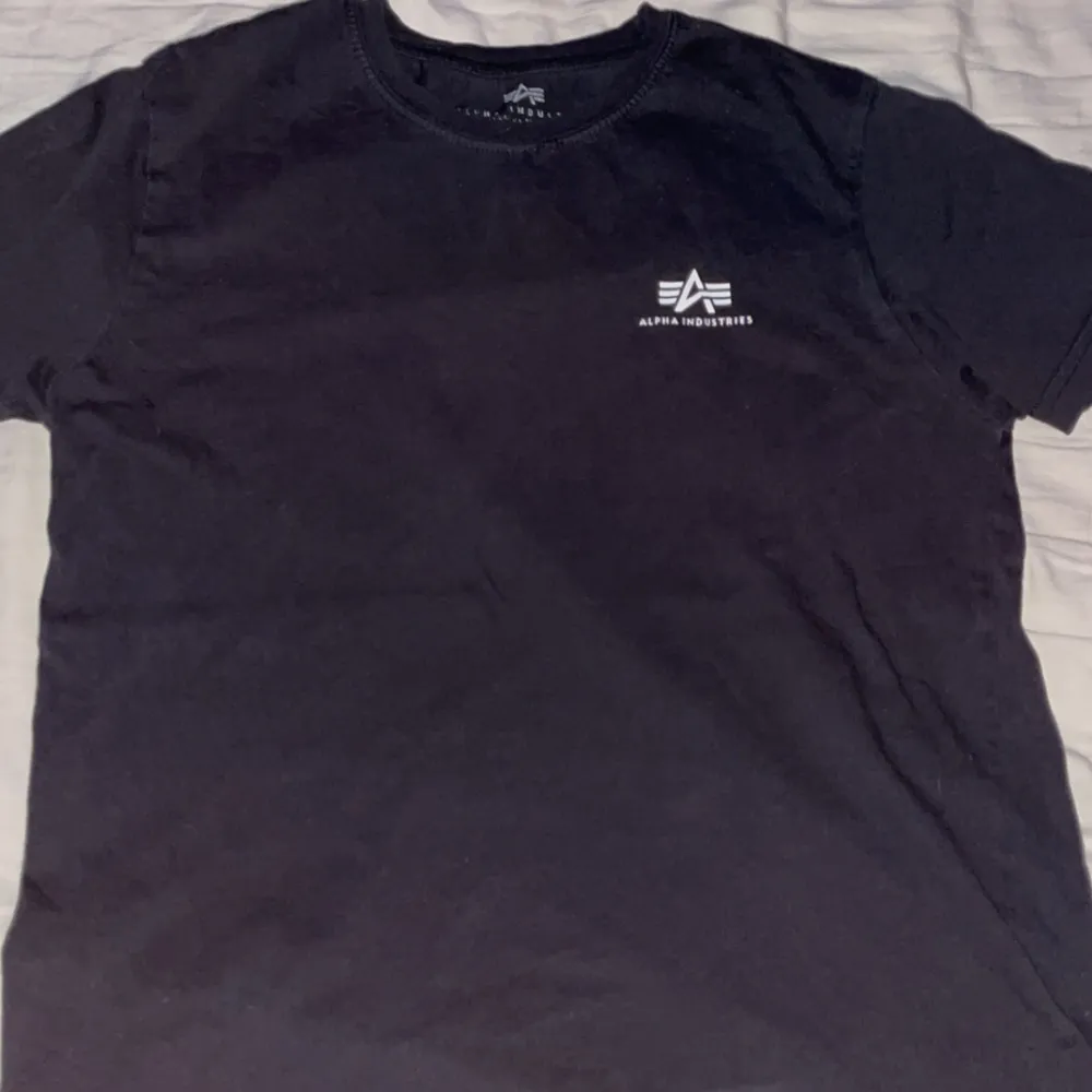 Säljer en stilren svart t-shirt från Alpha Industries. Den har en liten logga tryckt på bröstet och är tillverkad i ett mjukt material. Perfekt för en avslappnad look.. T-paidat.