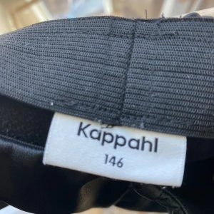 Svarta byxor från Kappahl - 45kr frakt 📦 ❗️                                     Snygga svarta byxor från Kappahl i storlek 146. Byxorna har en rak passform och är tillverkade i ett syntetmaterial som ger en glansig look. Perfekta för en stilren outfit. Skin/läder material 