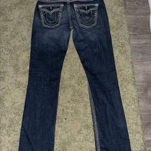 Mörkblå jeans från True Religion - Snygga mörkblå jeans från True Religion med kontrasterande vita sömmar. De har en straight passform och klassisk femficksdesign. Perfekta för en avslappnad stil. 