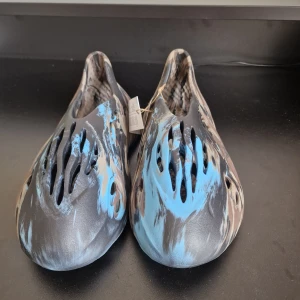 YEEZY FOAM RUNNER  - Säljer ett par Adidas Yeezy Foam Runner med ett unikt mönster i blått, beige och svart. Skorna har en futuristisk design med flera ventilationshål för extra komfort. Perfekta för en avslappnad stil.Har order bekräftelse från Adidas för att bevisa att de är äkta.