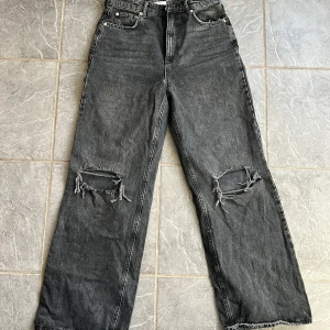 Svarta jeans med slitningar - Coola svarta jeans med slitningar på knäna. De har en klassisk femficksdesign och en rak passform som ger en avslappnad look. Perfekta för en trendig stil.