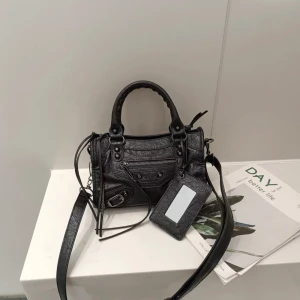 Svart axelväska med detaljer - Snygg svart axelväska med coola detaljer och en praktisk dragkedja. Väskan har både handtag och en justerbar axelrem för olika bärstilar. Perfekt för att ge din outfit en edgy touch. - 24 cm, aldrig använd