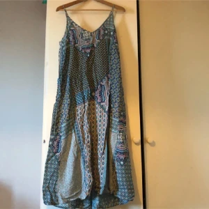 Mönstrad långklänning med snörning - Säljer en bohemisk långklänning med ett färgglatt mönster. Klänningen har en v-ringad hals och knytning i ryggen