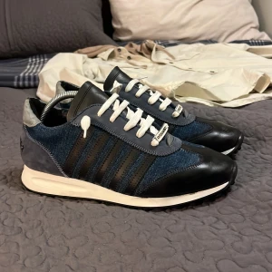 Blå sneakers från Dsquared2 - Snygga blå sneakers från Dsquared2 med svarta detaljer och vita snören. Skorna har en robust sula med bra grepp och är tillverkade i Italien. Perfekta för en stilren look. Nypris ca 2800 medan jag säljer de för endast 799. Skor är i otroligt bra skick och är använde väldigt lite. jag tar gärna emot byten och prisförslag vi hörs!!!