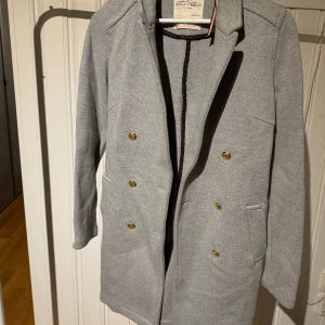 Grå kappa från Holly & Whyte - Snygg grå kappa från Holly & Whyte by Lindex med dubbelknäppning och stilrena detaljer. Perfekt för kyligare dagar med sin klassiska design och bekväma passform.