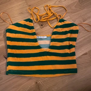 Randig croppad topp från Zara - Säljer en randig croppad topp från Zara i grönt och gult/orange. Toppen har smala axelband och en djup v-ringning. Perfekt för sommardagar!