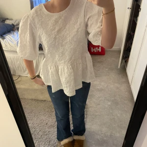 Vit blus med volangdetaljer - Säljer en söt vit blus med volangdetaljer och knytning i ryggen. Blusen har korta puffärmar och ett vackert texturerat mönster. Använd endast 1-2 gånger 