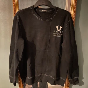 Svart tröja från True Religion - Säljer en svart tröja från True Religion med vit logga på bröstet. Tröjan har långa ärmar och ribbade muddar vid ärmslut och nederkant. Perfekt för en avslappnad stil. 🖤