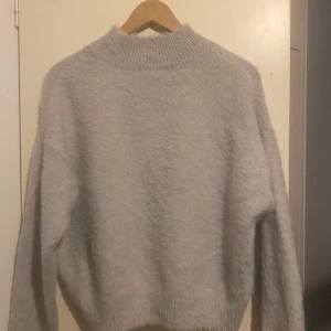 Grå fluffig tröja från H&M - Mysig och fluffig grå tröja från H&M. Perfekt för kyliga dagar med sin mjuka och varma känsla. Tröjan har en hög krage och långa ärmar, vilket gör den idealisk för både höst och vinter. En stilren och bekväm tröja för alla tillfällen.