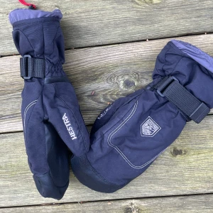 Svarta skidhandskar från Hestra - Säljer ett par svarta Hestra handskar med justerbara remmar och broderad logga. Perfekta för kalla dagar med sin varma och skyddande design. Storlek 6 enligt etiketten.
