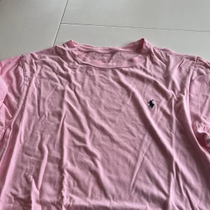 Rosa t-shirt från Polo Ralph Lauren - Säljer en snygg rosa t-shirt från Polo Ralph Lauren med det klassiska broderade logotypen på bröstet. Perfekt för en avslappnad stil. T-shirten är kortärmad och gjord i mjuk bomull.