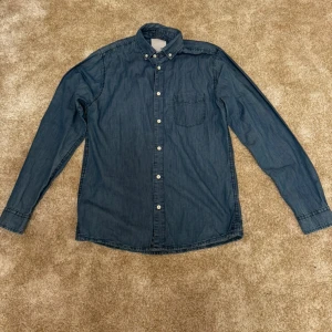 Blå jeansskjorta från Lager 157 - En stilren, långärmad jeansskjorta med knappar framtill och en bröstficka. Perfekt för en avslappnad men ändå välklädd look.  Kön: Herr Skick 9/10 Märke: Lager157 Storlek: S  Din stil: spara inlägget så du inte missar denna kappa Inte din stil: Kolla min profil. Du kommer hitta något för alla kön och åldrar.