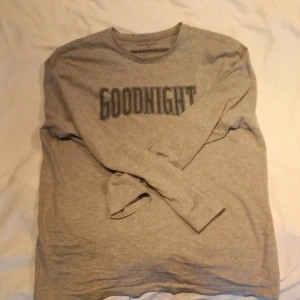 Grå långärmad tröja från Primark - Säljer en grå långärmad tröja från Primark med texten 'GOODNIGHT' tryckt på framsidan. Perfekt för en avslappnad look eller som mysplagg hemma. Tröjan är tillverkad i ett mjukt material för extra komfort.