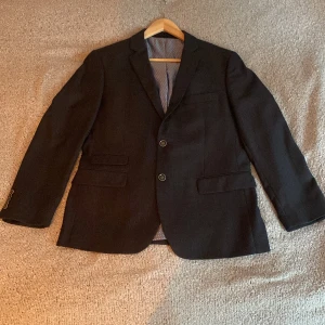 Svart kavaj från Seattle - Snygg svart kavaj från Seattle med två knappar framtill och klassiska fickor. Insidan har ett stilrent prickigt foder. Perfekt för en elegant look.