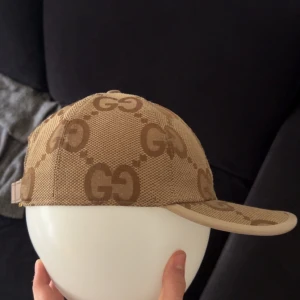 Beige keps med GG-mönster - Snygg beige keps med det ikoniska GG-mönstret. Perfekt för att ge din outfit en lyxig touch. Justerbar passform för optimal komfort.