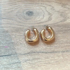 Guldiga örhängen i chunky design - Snygga guldiga örhängen i en chunky och modern design. Perfekta för att ge en stilren touch till din outfit. De har en slät och glänsande yta som fångar ljuset fint.