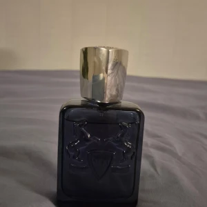 Parfym Parfums de Marly Sedley - Säljer denna sommar paefym från Parfums de Marly, modellen Sedley. Flaskan är mörkblå med en silverfärgad kork och har en stilren design med två hästar i relief. Förpackningen är i matchande blå nyans. Perfekt för den som söker en lyxig doftupplevelse, 75ml. Det är ungefär 96% kvar.