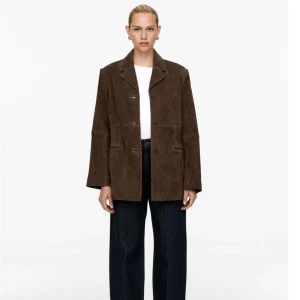 Brun mockakavaj ARKET - Snygg brun mockakavaj med klassisk krage och knappar framtill. Perfekt för en stilren look. Kavajen har långa ärmar och två fickor framtill.             Fodrad. Avskärningar både fram och bak samt passpoalfickor.                                               MATERIAL OCH LEVERANTÖRER Mocka 100% Foder: Viskos 100%                                                          Storlek 34.  ( kan passa en 36) då den har lös passform. ORDINARIE PRIS 5500 SEK