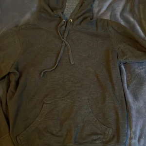 mörk grå hoodie - Säljer en klassisk mörk grå hoodie med justerbar dragsko i huvan och en praktisk magficka. Perfekt för en avslappnad stil och passar till det mesta. Hör av dig vid intresse!