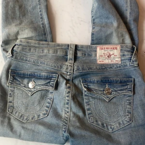 Blå bootcut jeans från True Religion - Snygga blå bootcut jeans från True Religion med medelmidja. Klassisk femficksdesign med dekorativa sömmar och knappar på bakfickorna. Perfekta för en avslappnad stil. Använda fåtal gånger. Tvättas innan jag postar. Pris: 1000kr  nypris: 1299kr. Pris kan diskuteras💞