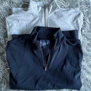 Grå och marinblå tröja från Bondelid - Två stilrena tröjor från Bondelid i storlek S. Den ena är grå och den andra marinblå, båda med dragkedja vid halsen. Perfekta för en avslappnad och bekväm stil. 
