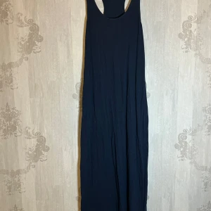 Mörkblå långklänning från H&M - Säljer en stilren mörkblå långklänning från H&M. Klänningen har en enkel design med ärmlös stil och rund halsringning. Perfekt för en avslappnad look eller att klä upp med accessoarer. Tillverkad i ett mjukt och bekvämt material.