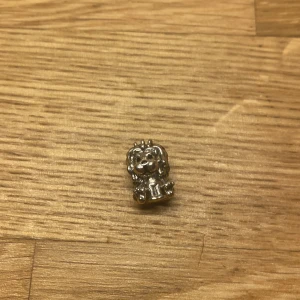 Silverfärgad berlock med lejonmotiv - En söt och detaljerad silverfärgad berlock föreställande ett lejon. Perfekt för att fästa på ett armband eller halsband för en personlig touch. Lejonet har en Union Jack-detalj vid basen, vilket ger en unik och stilfull look.