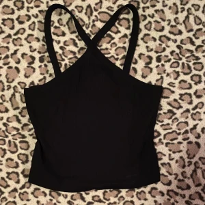 Svart topp - Snygg svart topp med korsade axelband. Toppen är figurnära och har en enkel design som passar till många olika outfits.