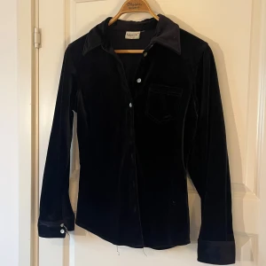Svart Sammets Skjorta! - Ett av mina gamla favoritplagg som jag inte använder längre! Överlag i bra skick utom ett par trådar och trasig knapp, därav priset! Skjortan är köpt från myrornas och är från märket Cappuccini✨100% Polyester och storlek uppskattas vara ungeför S 