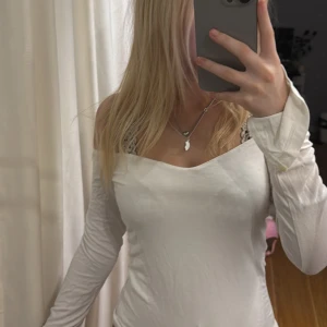 Vit långärmad topp - Säljer en stilren vit långärmad topp med en offshoulder design. Perfekt för att matcha med olika outfits. Toppen har en åtsittande passform som framhäver figuren.