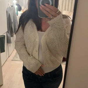 Beige stickad kofta - Säljer en beige stickad kofta med ett fint hålmönster. Koftan har långa ärmar och knappar framtill. Perfekt för att lägga till en mysig touch till din outfit. Säljer då jag inte använder den och den är som ny 