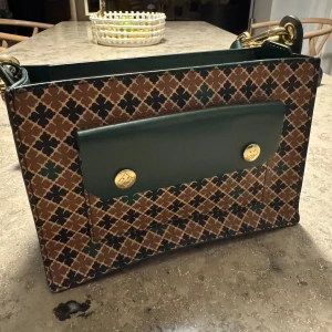 By Malene Birger väska - Snygg axelväska med ett rutigt mönster i brunt, beige och grönt. Väskan har gröna detaljer och en praktisk dragkedja. Perfekt för att ge din outfit en unik touch.