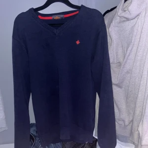 Mörkblå tröja från Morris - Säljer en stilren mörkblå tröja från Morris i 100% bomull. Tröjan har en v-ringad design med en liten röd broderad logotyp på bröstet. Perfekt för en avslappnad men ändå snygg look. Finns en defekt på tröjan men är väll ihop syd kolla bild 5. Därav det lägre priset