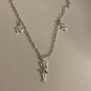 Silverfärgat halsband med stjärnor och figur - Charmigt silverfärgat halsband med en kedja som har två små stjärnor och en central figur. Perfekt för att lägga till en lekfull touch till din stil.