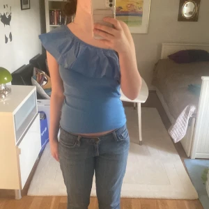 Blå oneshoulder topp med volang - Snygg blå oneshoulder topp med volangdetalj. Perfekt för en somrig look. Toppen har en tight passform och är tillverkad i ett mjukt material. Använd 1 gång💕